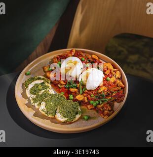 Moderno caffè che serve un pasto delizioso e salutare di shakshuka con uova in camicia e bruschetta al pesto Foto Stock