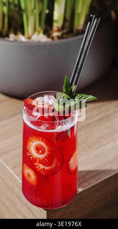 Cocktail di fragole rosse con cubetti di ghiaccio e foglie di menta fresca in piedi su un tavolo di legno Foto Stock