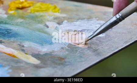 L'artista mescola le vernici a olio sulla tavolozza con il pennello per creare un nuovo colore Foto Stock