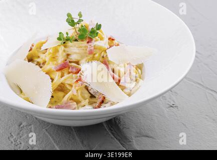 Pasta cremosa alla carbonara servita in una moderna ciotola bianca, con prezzemolo fresco e scaglie di parmigiano Foto Stock
