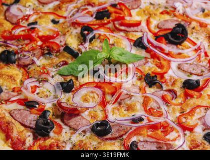Pizza al peperoni appena sfornata con olive, cipolle e basilico da vicino Foto Stock
