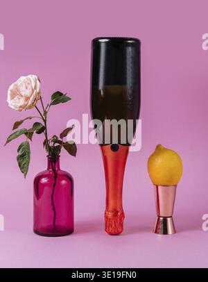 Natura morta minimale con una rosa, una bottiglia di vino e un limone su un vivace sfondo rosa Foto Stock