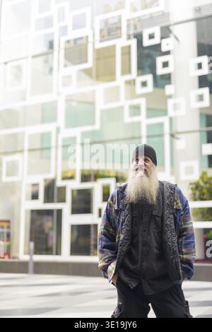 Ritratto di un uomo hipster barbuto maturo contro il muro con un design astratto nelle strade della città all'aperto Foto Stock