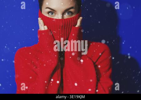 Donna sorpresa con dolcevita rossa che si prepara per la stagione invernale con uno sfondo blu brillante Foto Stock