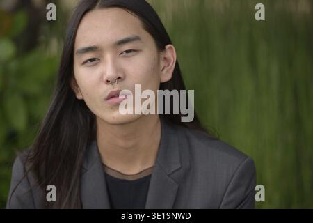 Ritratto di un giovane uomo d'affari asiatico con i capelli lunghi che indossa una tuta al parco all'aperto Foto Stock