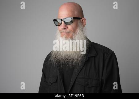 Foto in studio di un uomo calvo bello e maturo con una lunga barba bianca su sfondo grigio Foto Stock