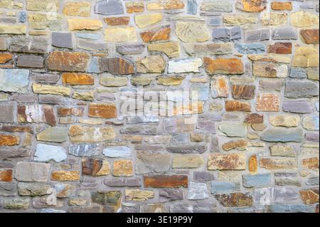 Pareti in pietra testurizzata con vari colori e forme irregolari che creano una facciata rustica Foto Stock