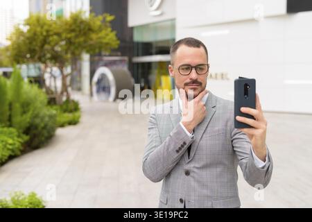 Ritratto di un uomo d'affari ispanico con la barba calva che indossa un abito nelle strade della città all'aperto Foto Stock