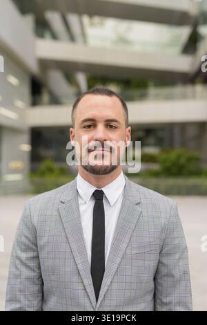 Ritratto di un uomo d'affari ispanico con la barba calva che indossa un abito nelle strade della città all'aperto Foto Stock