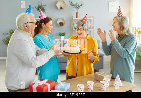 Gli anziani festeggiano il compleanno con una torta, condividendo momenti di gioia con l'infermiera premurosa nella casa di riposo. Foto Stock