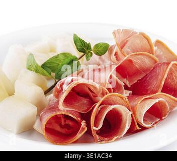 Fette di prosciutto con melone di cantaloupe su un piatto bianco guarniggendo con menta fresca Foto Stock
