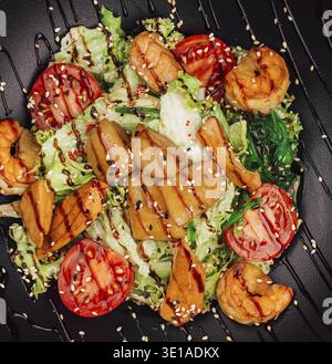 Deliziosa insalata con gamberetti alla griglia, capesante scottate, salmone e verdure servite su un piatto nero Foto Stock