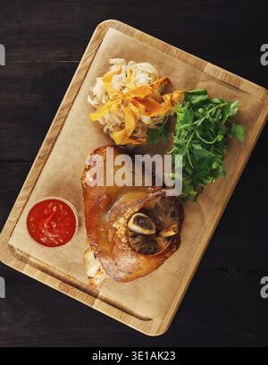 Le nocche di maiale croccanti sono servite su un tavolo di legno con insalata, crauti e salsa Foto Stock