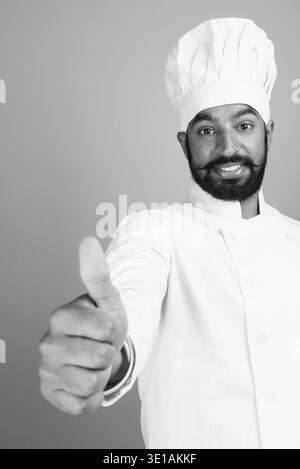 Foto in studio di un giovane e bell'indiano barbuto come chef su sfondo grigio in bianco e nero Foto Stock