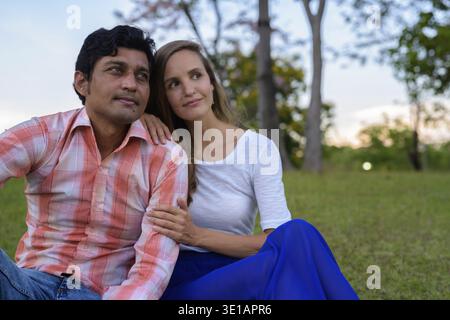 Multi etnico giovane seduto e il pensiero sul prato in amore al tranquillo parco verde Foto Stock