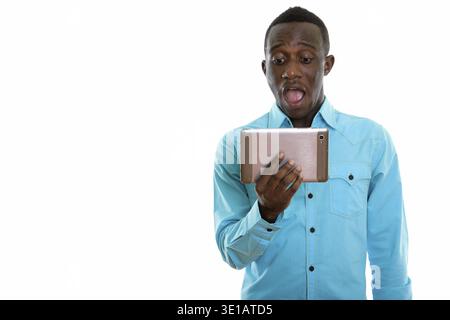 Studio shot del giovane africano nero uomo con tavoletta digitale mentre lo sguardo scioccato Foto Stock