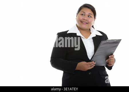 Riflessivo giovani felici fat Asian imprenditrice sorridente e guardando verso l'alto tenendo negli appunti Foto Stock