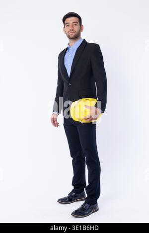 Foto in studio di un giovane e bellissimo uomo d'affari persiano barbato in tuta con elmetto isolato su sfondo bianco Foto Stock