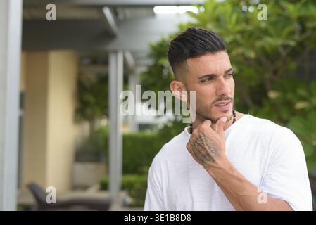 Ritratto di giovane uomo persiano bello con barba stoppia con la natura nel giardino sul tetto all'aperto Foto Stock