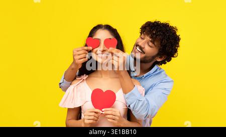 Coppia che si diverte con le forme del cuore nella parte anteriore dello sfondo giallo brillante Foto Stock