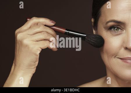 Bella donna di mezza età applicando polvere di fondazione o arrossire sul suo viso Foto Stock