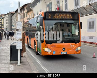 Autobus della linea 2 che arriva a Pisa, Italia. La donna aspetta alla fermata dell'autobus accanto agli edifici storici, luogo di transito urbano comune europeo. Foto Stock