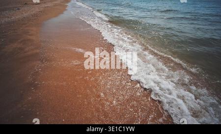 Onde delicate che scivolano su sabbia dorata su una spiaggia soleggiata in crimea, creando un paesaggio marino tranquillo e invitante Foto Stock