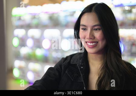 Felice giovane donna asiatica che gioca videogiochi arcade al chiuso Foto Stock