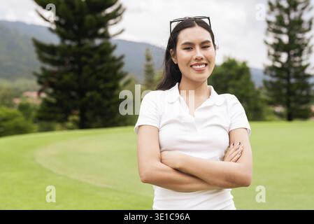 Giovane donna asiatica sul campo da golf che indossa una polo bianca e si rilassa sul campo verde. Vacanze estive o svago a tema con un elegante stile di vita Foto Stock
