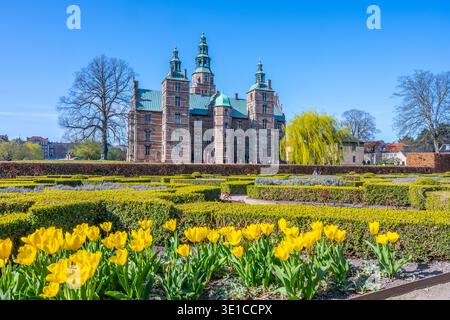 Il castello di Rosenborg si erge maestosamente a Copenaghen, Danimarca, incorniciato da vibranti tulipani gialli e vegetazione lussureggiante. I visitatori apprezzano l'atmosfera serena in una giornata primaverile limpida. Foto Stock