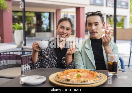Amici felici che mangiano pizza insieme e fanno mini gesti cardiaci sorridendo Foto Stock
