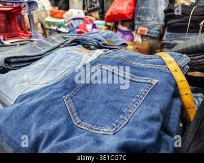 Primo piano di jeans blu con un metro a nastro giallo disposto sulla vita della coppia superiore nell'espositore impilato del mercato centrale, Phnom Penh Foto Stock
