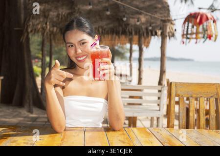 Giovane donna che beve anguria in spiaggia in Thailandia Foto Stock