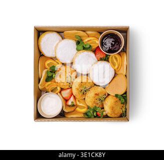 Una scatola da dessert offre una varietà di dolci, tra cui soffici pancake, purea di mango tropicale e fragole fresche. Completata da salse, è così Foto Stock