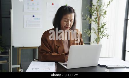 Maturo business asiatico donna imprenditrice in ufficio che utilizza laptop. donna d'affari degli anni '60 con donna anziana asiatica di tecnologia Foto Stock