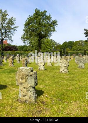 Antico cimitero con numerose croci di pietra e lapidi sparsi su erba verde sotto il cielo blu. Gli alberi maturi forniscono un backdr naturale Foto Stock