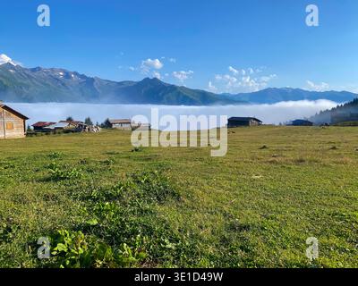 Scenografico paesaggio alpino con prati verdi punteggiati da tradizionali casali in pietra, adagiati su spettacolari montagne avvolte da bassa nebbia e Foto Stock