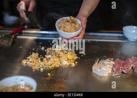Le mani dello chef con la spatola sopra il teppanyaki. cucinare verdure, carne e pesce su un tavolo caldo per grigliate hibachi. Cucina tradizionale giapponese. Spettacolo Teppan Foto Stock