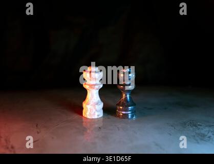 Un pezzo da scacchi da re con trama in marmo bianco e un pezzo da scacchi da regina lucido nero si stagliano fianco a fianco su una superficie in pietra intemprata. Un'illuminazione straordinaria crea contrasto Foto Stock
