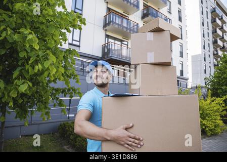 Uomo di consegna forte che tiene una pila di scatole di cartone su una strada della città Foto Stock