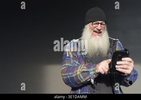 Ritratto di un uomo hipster barbuto maturo contro un muro nero all'aperto Foto Stock
