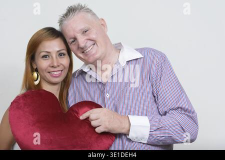 Foto in studio di un uomo anziano e una donna asiatica matura in coppia insieme e innamorata su sfondo bianco Foto Stock