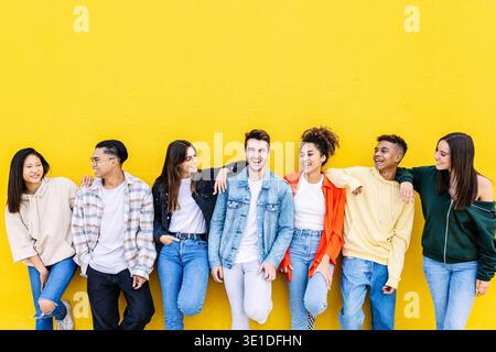 Comunità giovanile. Gruppo di amici diversi che si trovano insieme sopra il muro giallo Foto Stock