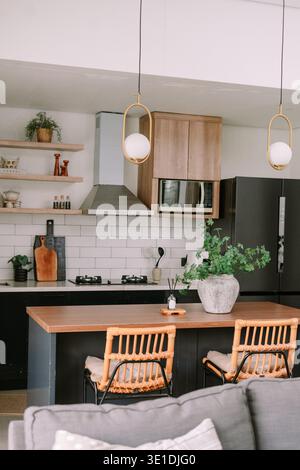 Gli interni eleganti e invitanti della cucina moderna presentano un'isola di legno con sgabelli da bar in rattan e decor minimalista. Le luci a sospensione illuminano il dispositivo sle Foto Stock