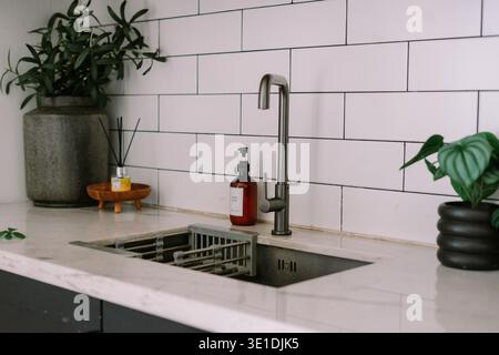 Moderna area lavabo con un elegante rubinetto in acciaio inossidabile, ripiano in marmo e spruzzi di piastrelle bianche della metropolitana. Dispenser e recipiente per sapone per le mani elegante Foto Stock
