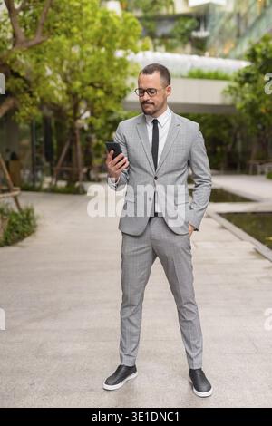 Ritratto di un uomo d'affari ispanico con la barba calva che indossa un abito in città con la natura all'aperto Foto Stock