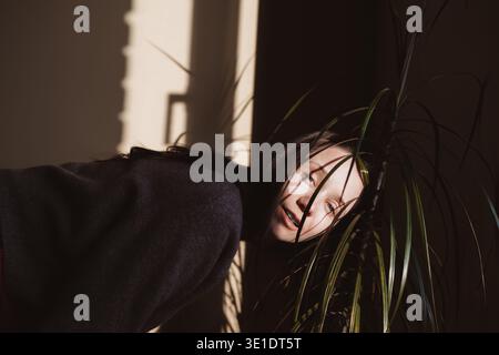 Moody ritratto cinematografico di una donna che guarda attraverso foglie di palma verdi. Gioco d'ombra creativo, emozione autentica, consapevolezza della salute mentale e sole duro Foto Stock