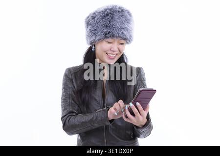 Foto in studio di una bellissima donna asiatica che indossa un cappello di pelliccia pronto per l'inverno isolato su sfondo bianco Foto Stock