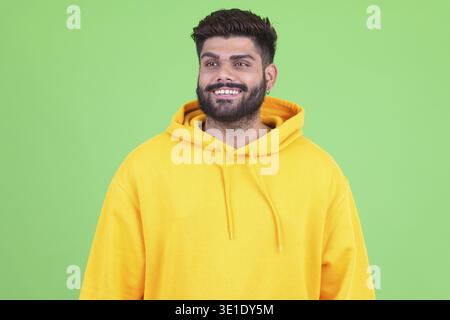 Foto in studio di un giovane indiano con barba in sovrappeso che indossa una felpa con cappuccio su chiave cromatica con sfondo verde Foto Stock