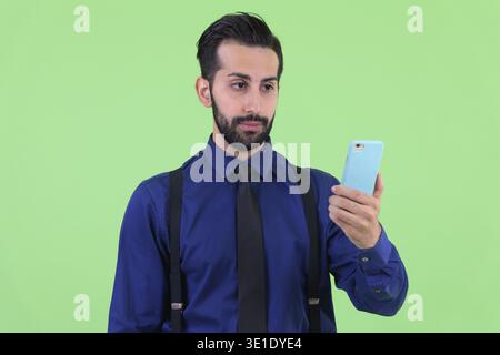Foto in studio di un giovane e bellissimo uomo d'affari persiano barbato su sfondo verde Foto Stock
